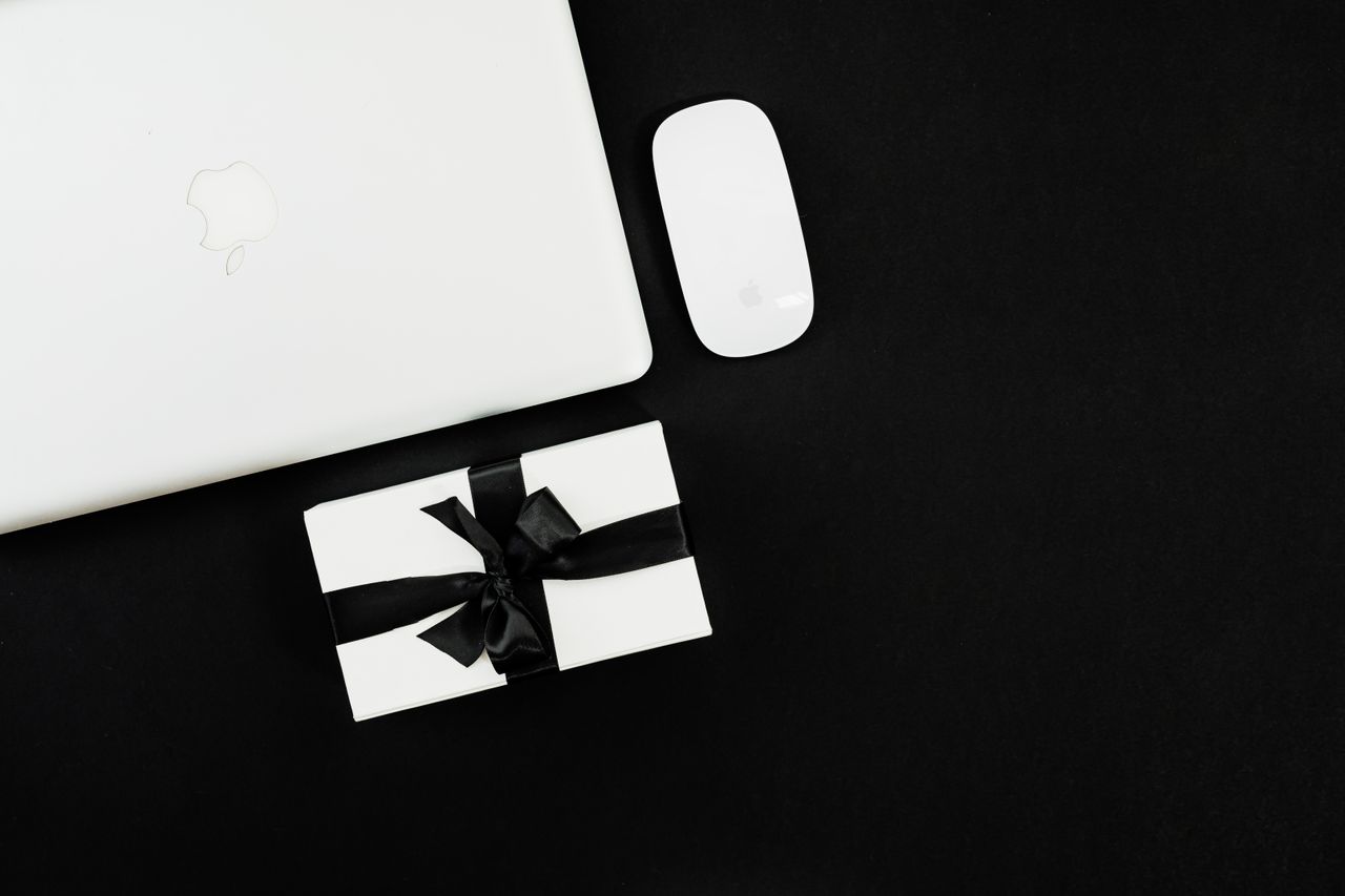 Flat lay of a laptop, mouse, and gift box, ideal for Black Friday online shopping theme.